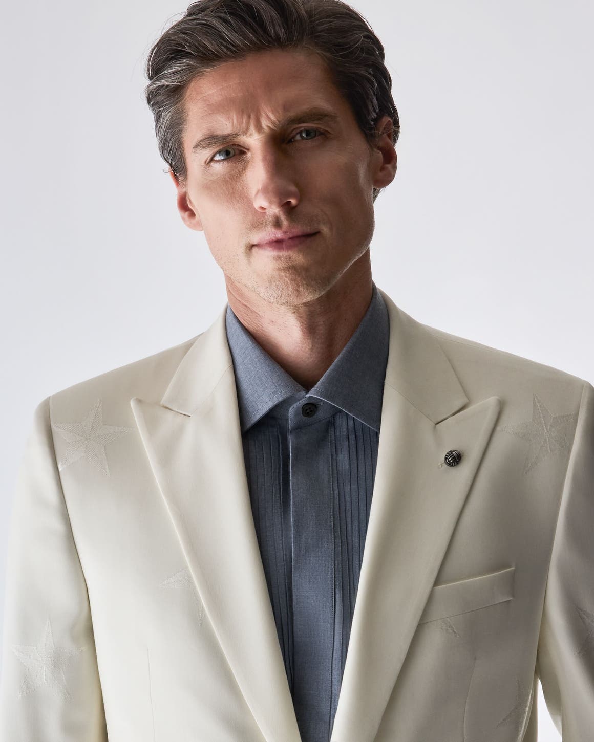 A man wearing a beige suit-blazer and grey shirt from Jack Victor.