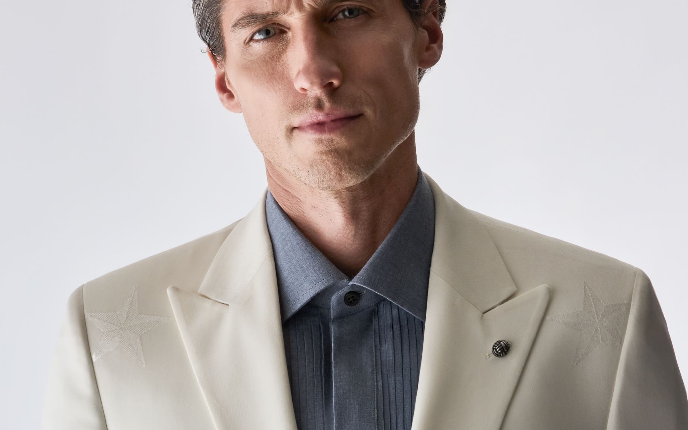 A man wearing a beige suit-blazer and grey shirt from Jack Victor.