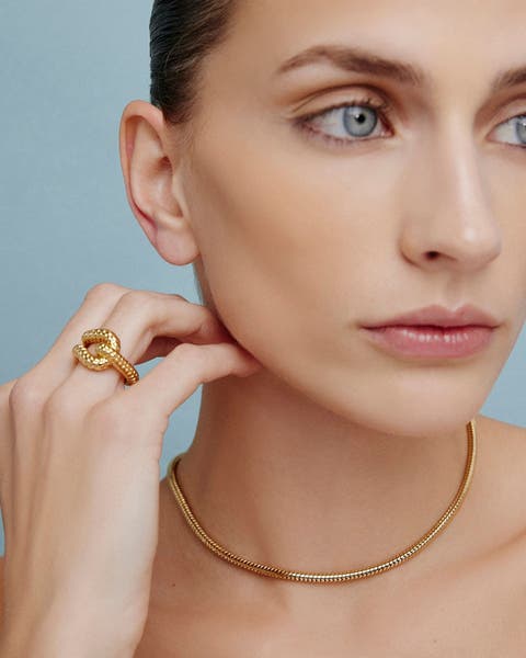 A woman wearing a gold necklace and ring.