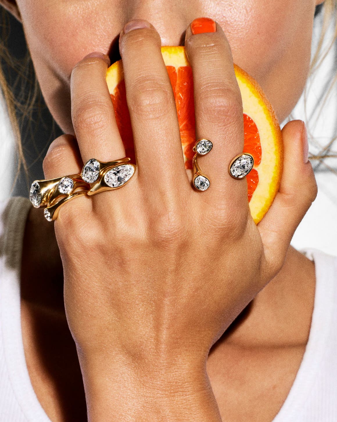 A woman holding an orange with John Hardy diamond rings stacked on three fingers.