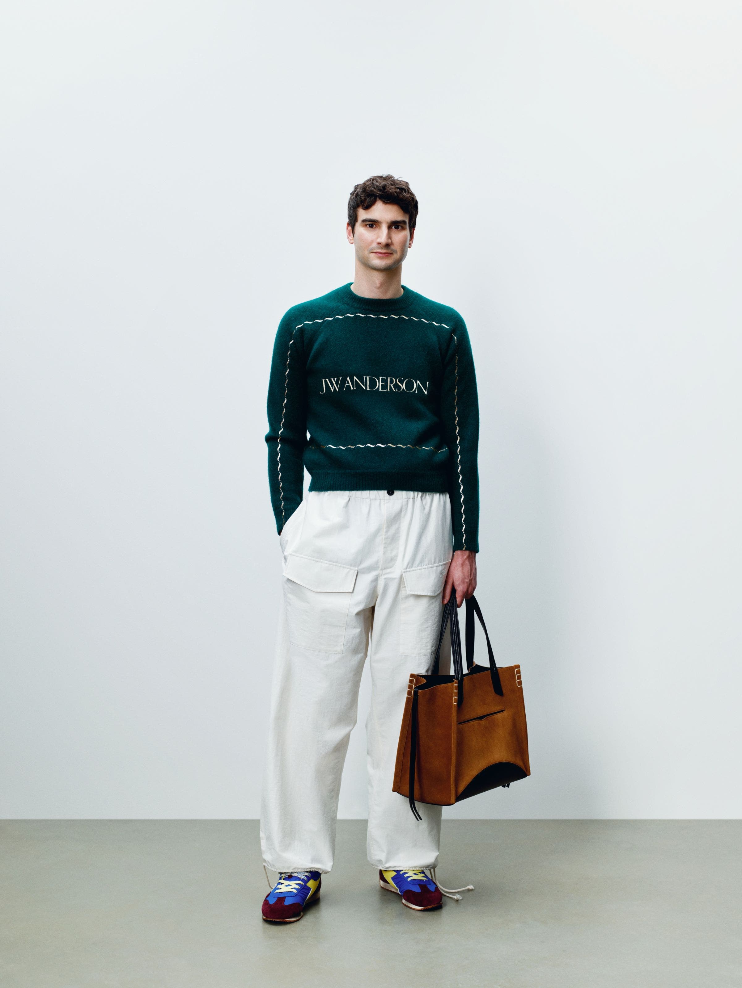 A man wearing low-top sneakers with white cargo pants and a green sweater.