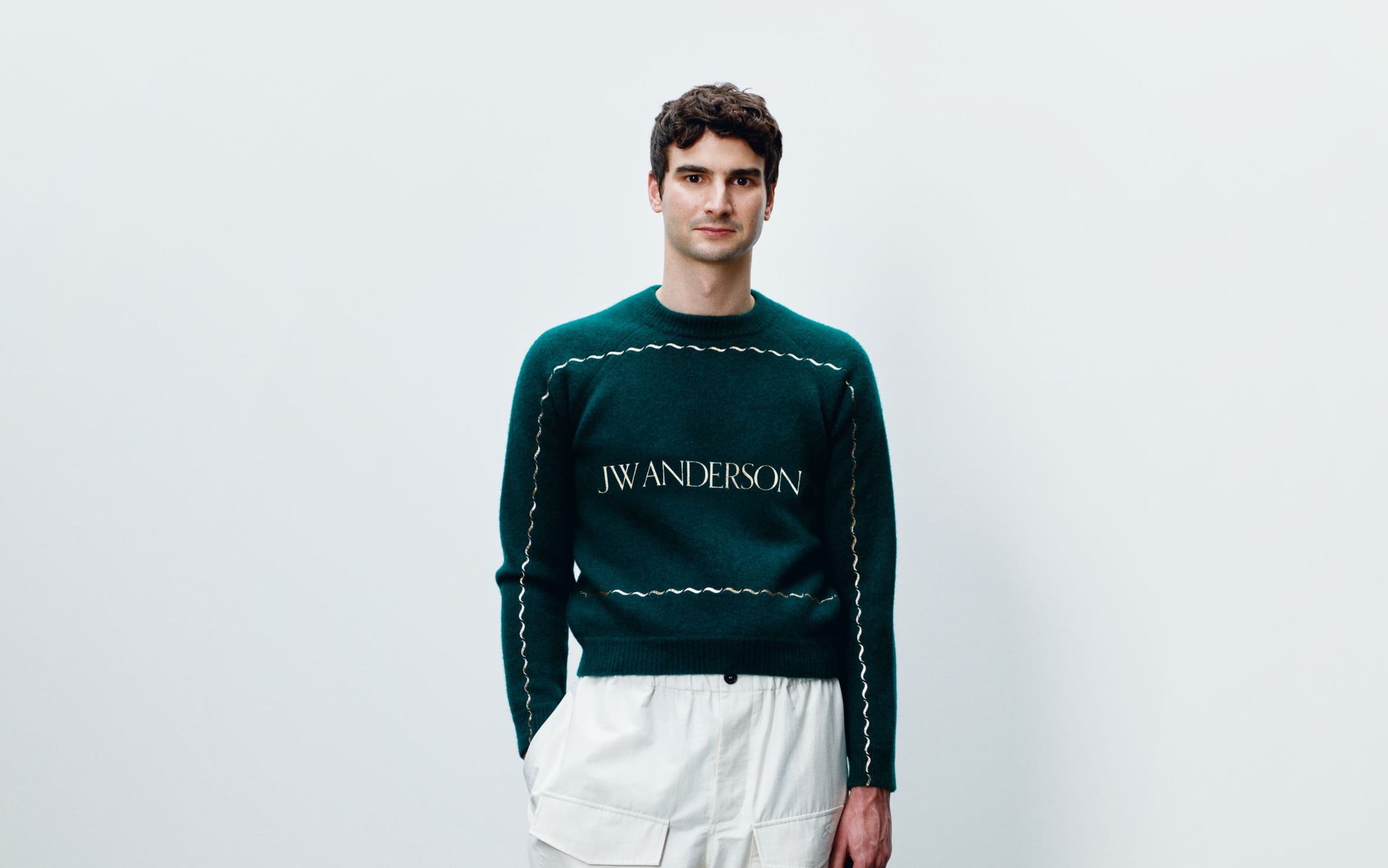A man wearing low-top sneakers with white cargo pants and a green sweater.