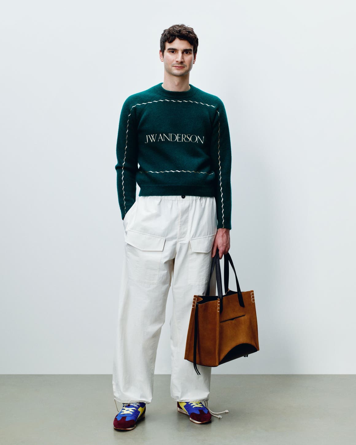 A man wearing low-top sneakers with white cargo pants and a green sweater.