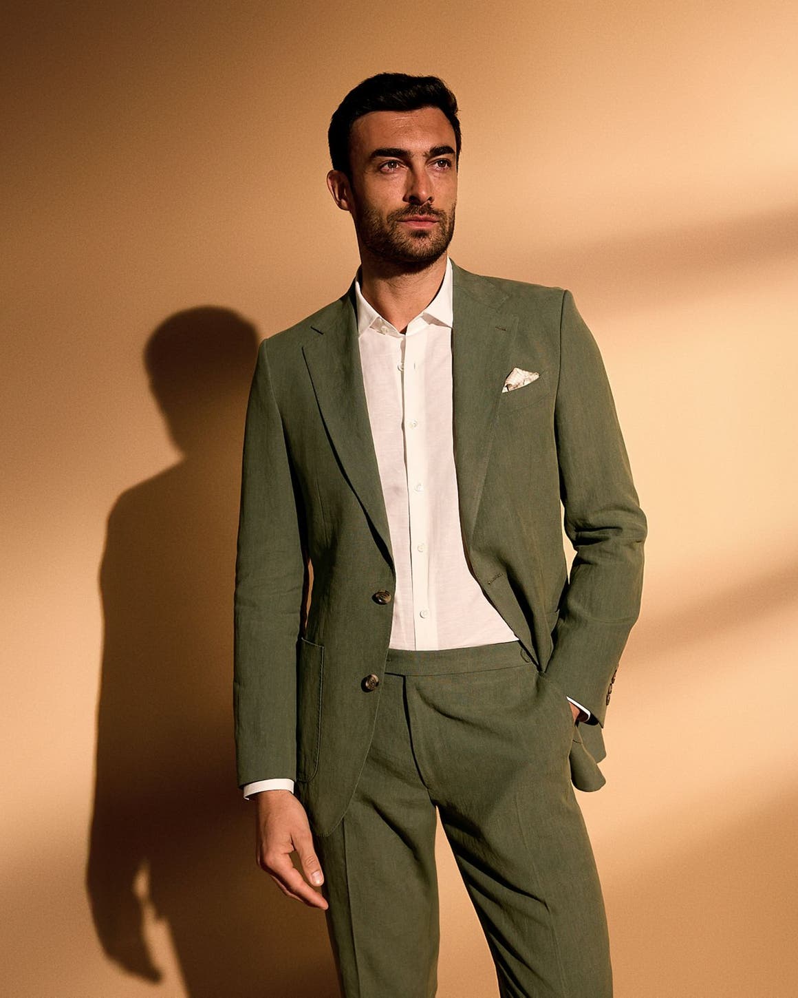 A man wearing an olive suit and white button-up.