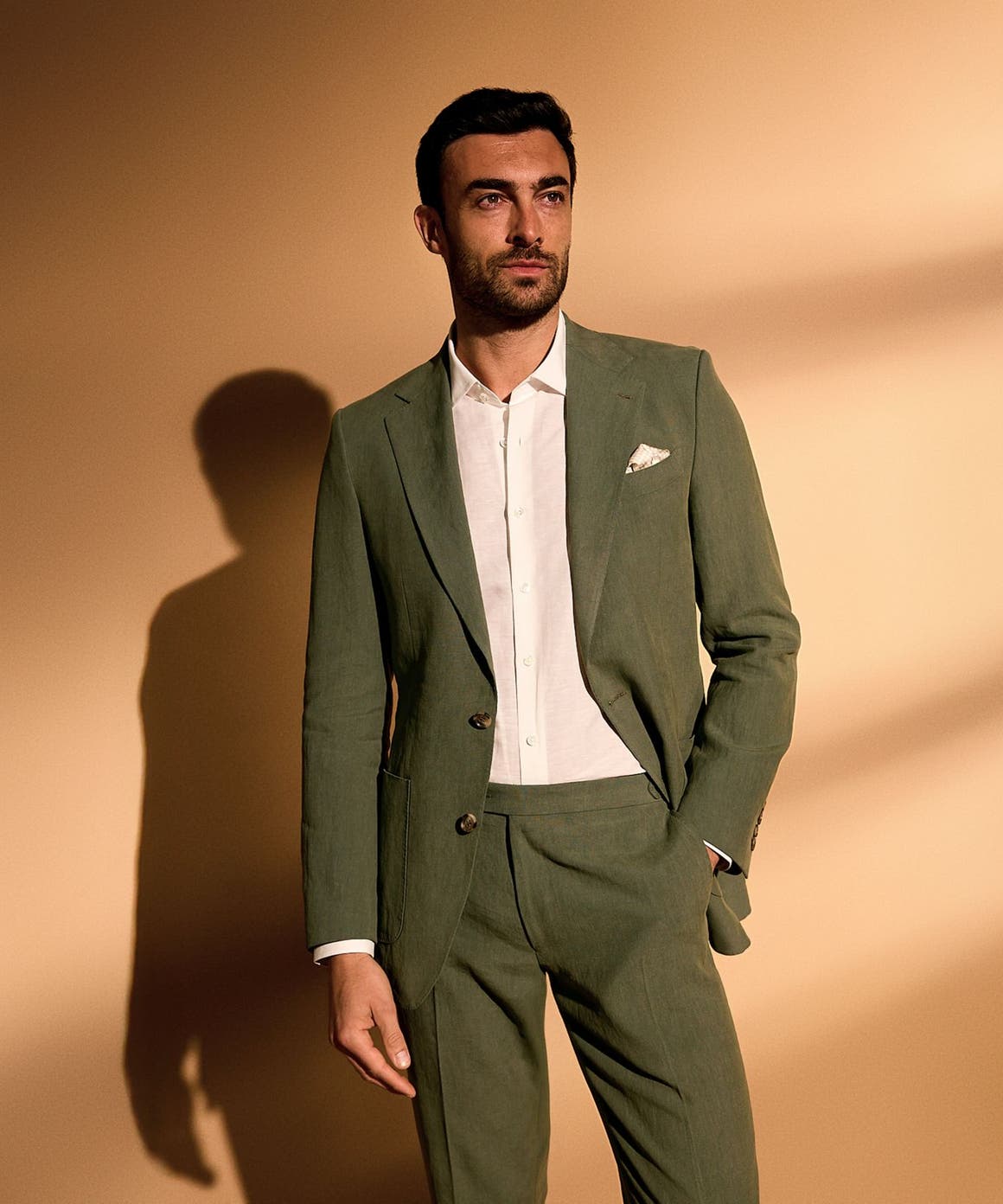 A man wearing an olive suit and white button-up.