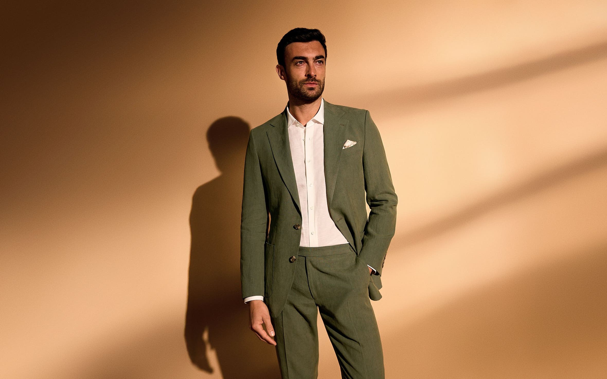 A man wearing an olive suit and white button-up.