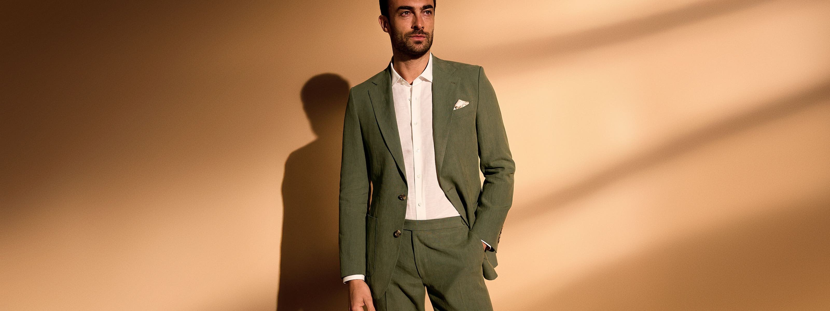 A man wearing an olive suit and white button-up.