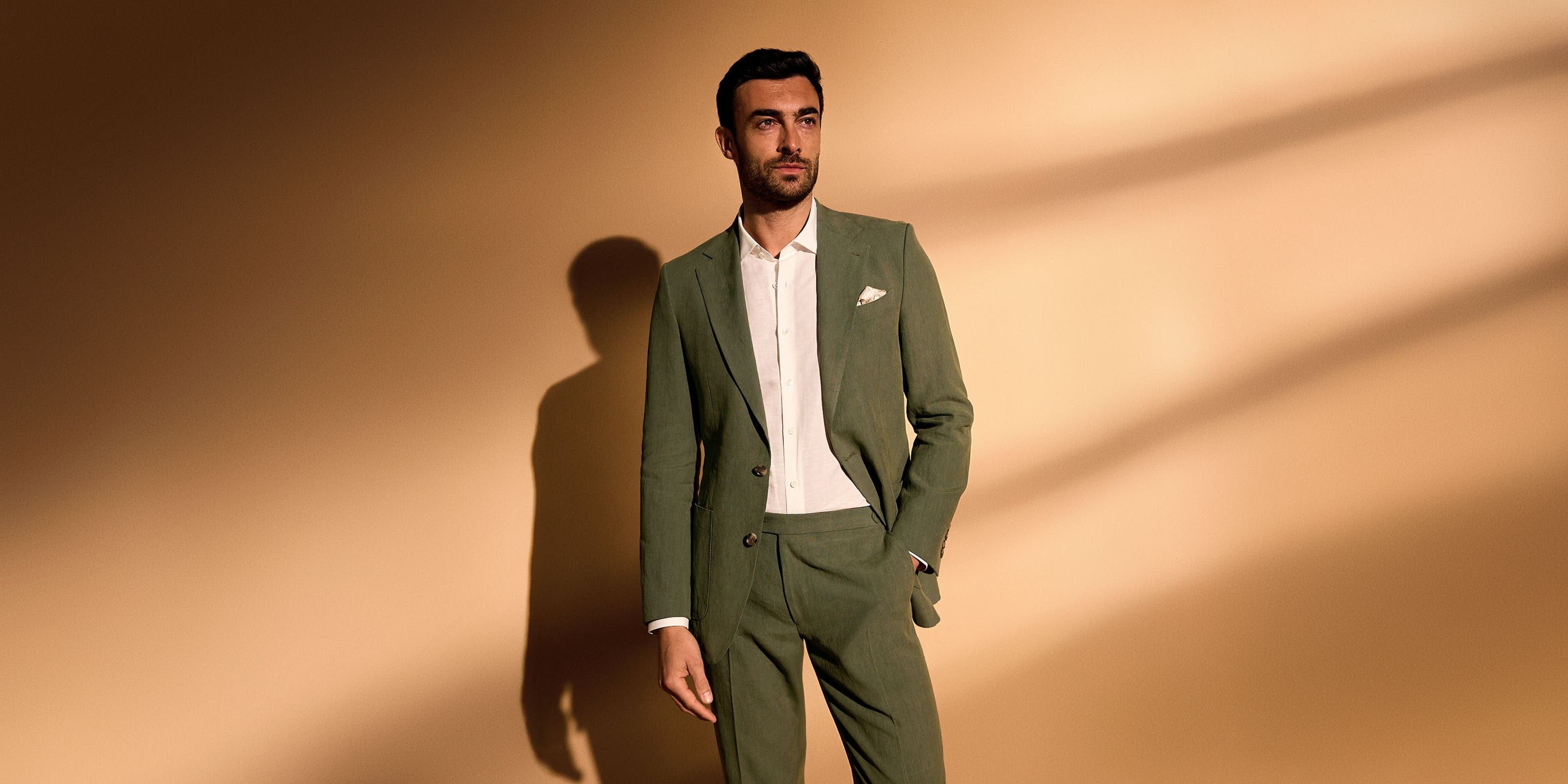 A man wearing an olive suit and white button-up.