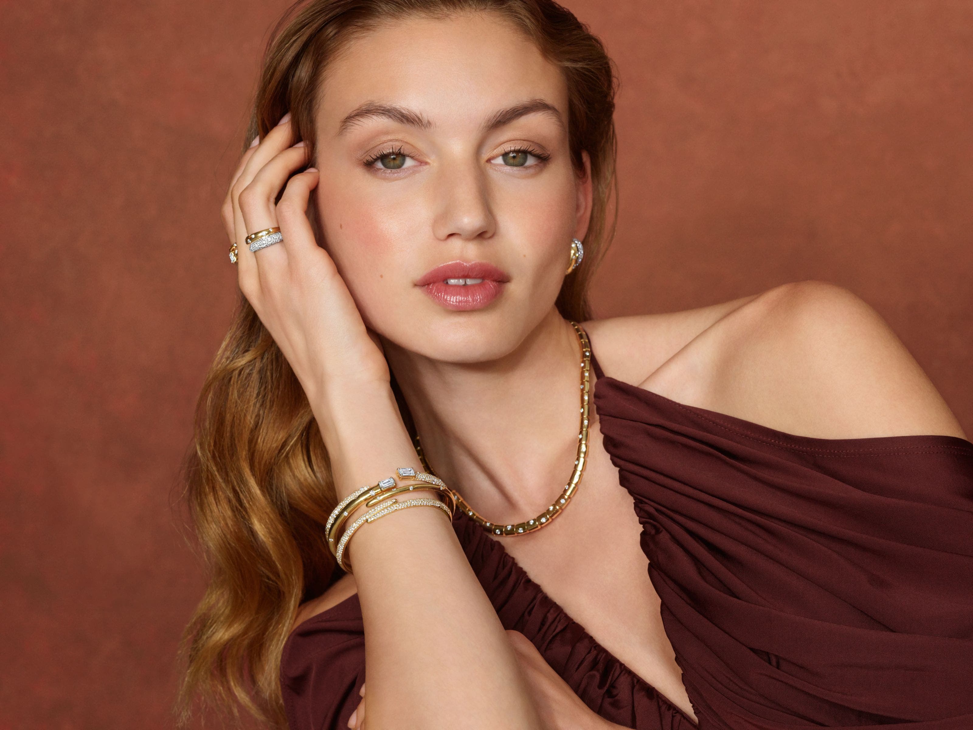 A woman wearing a variety of gold and diamond bracelets, earrings and rings. 