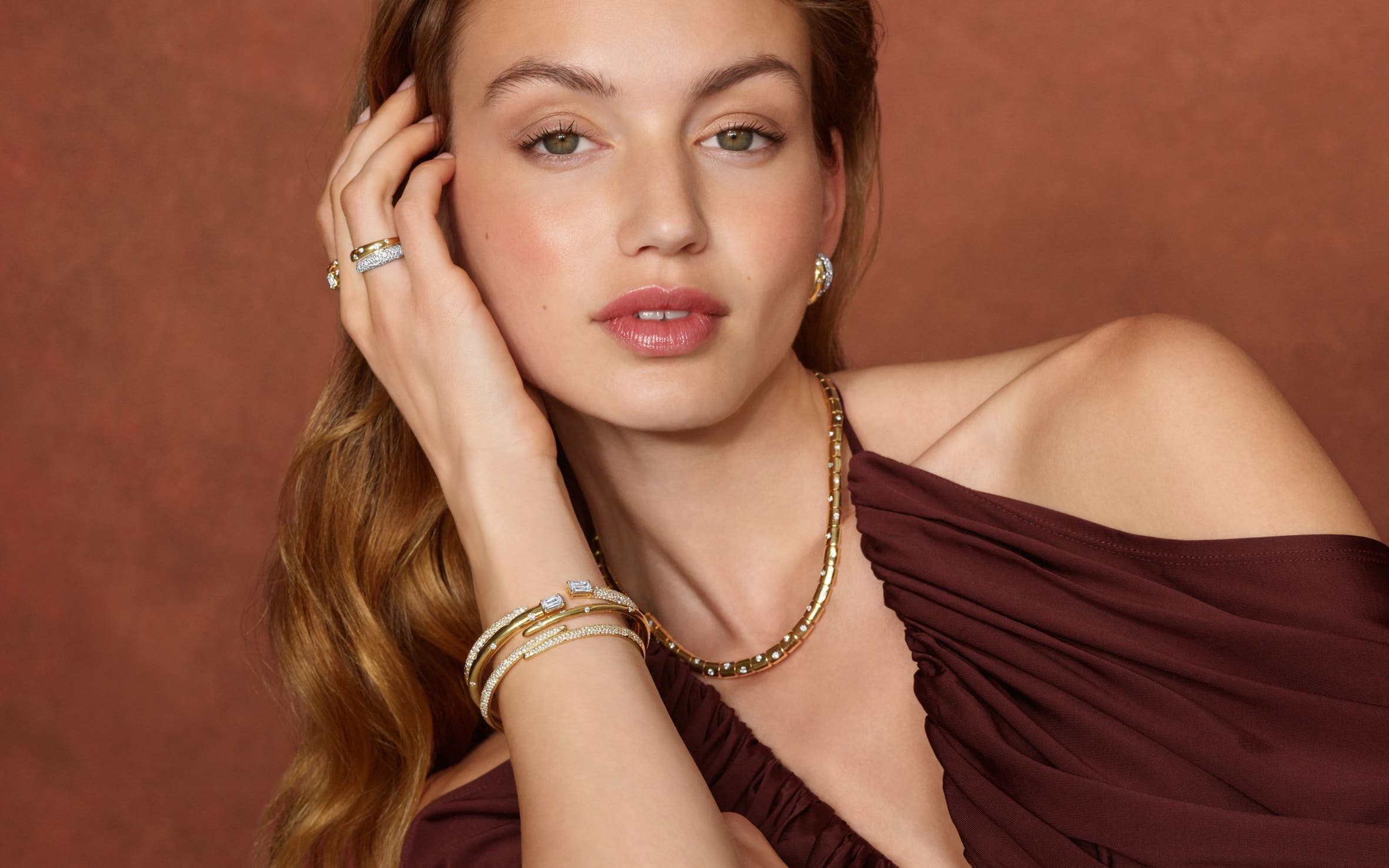 A woman wearing a variety of gold and diamond bracelets, earrings and rings.