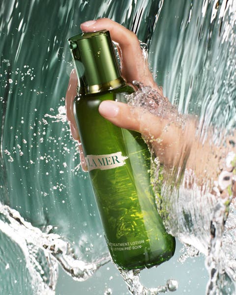 Hand holding a green La Mer bottle, surrounded by splashing water.