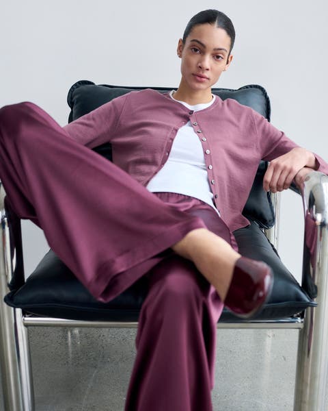 A woman wearing a magenta cardigan with a white shirt and silk pants.