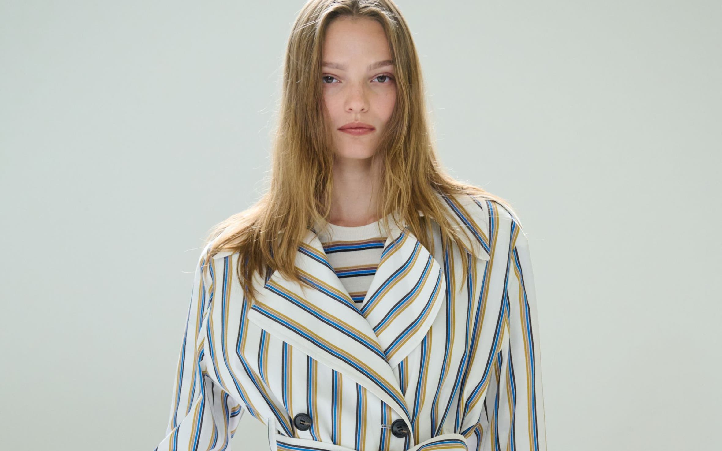 A woman wearing a striped trenchcoat and matching pants over a striped top.