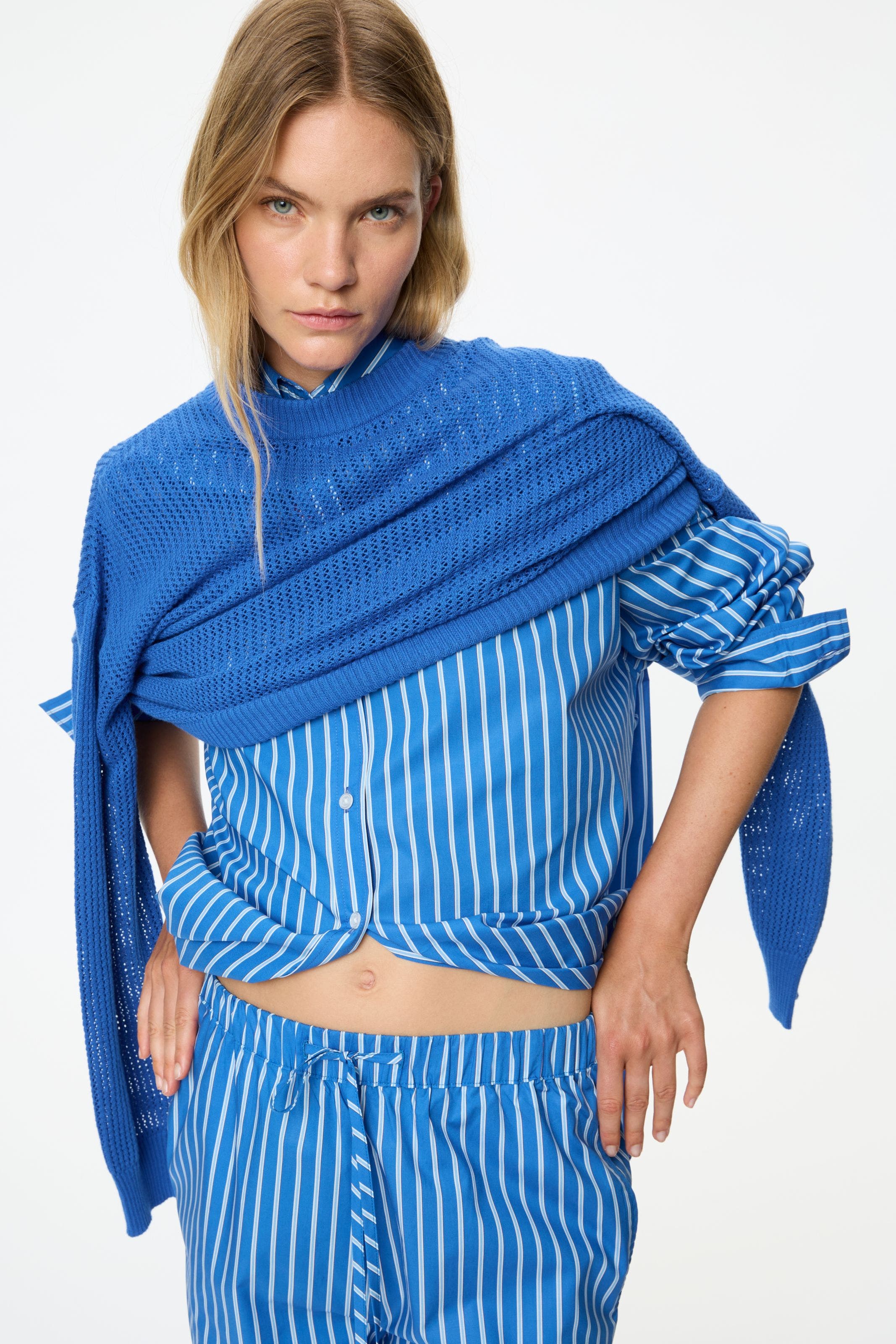 A woman wearing a blue and whited button up, matching pants, and a blue pullover sweater.