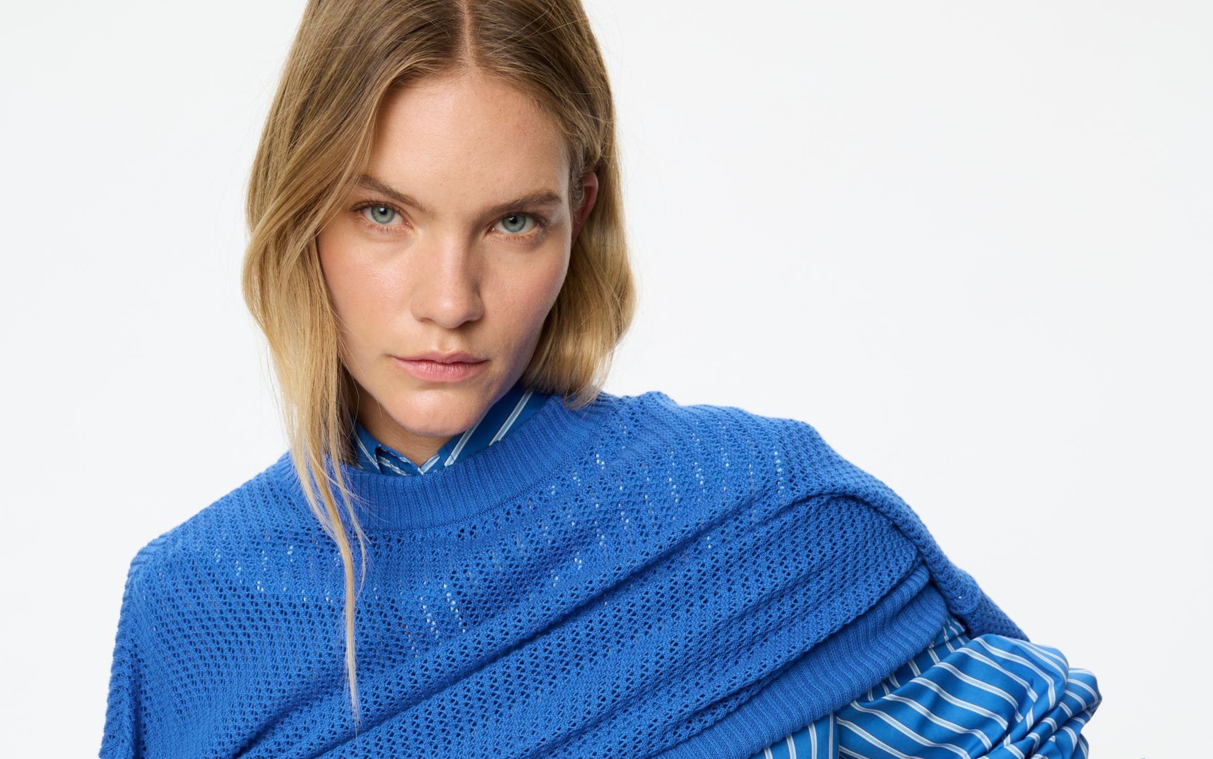 A woman wearing a blue and whited button up, matching pants, and a blue pullover sweater.