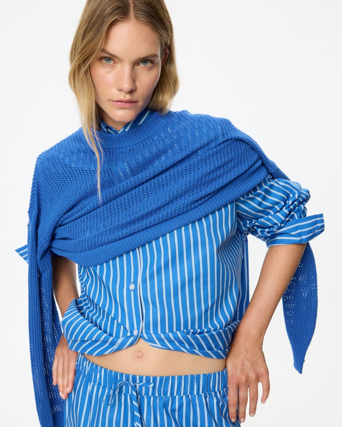A woman wearing a blue and whited button up, matching pants, and a blue pullover sweater.