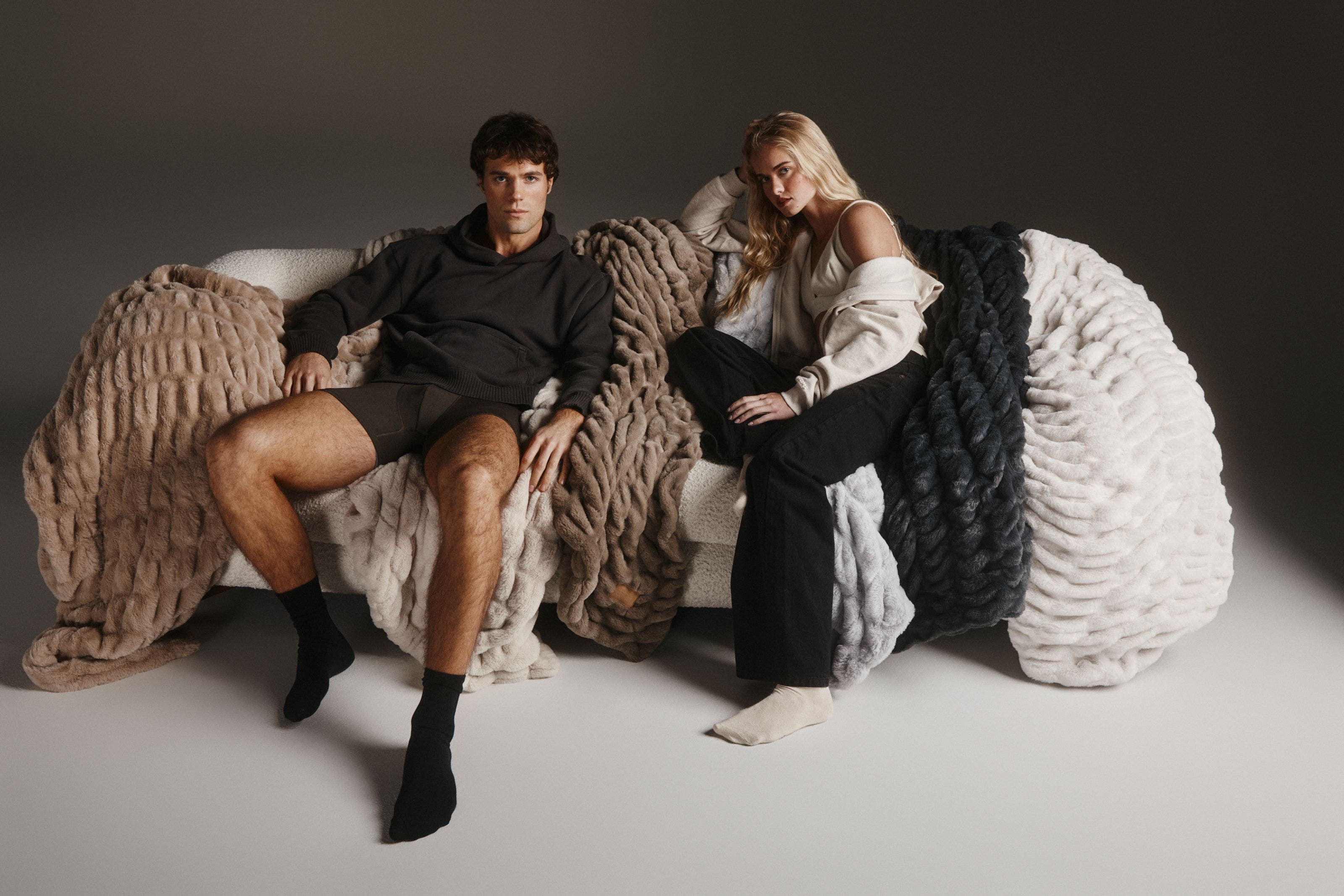 A man and a woman relaxing on chunky knit blankets.