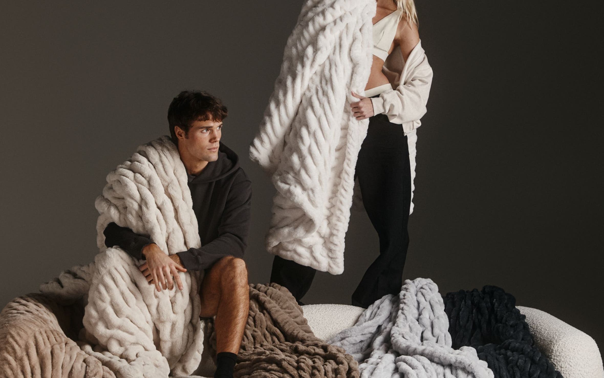 Man and woman standing on couch with blankets.