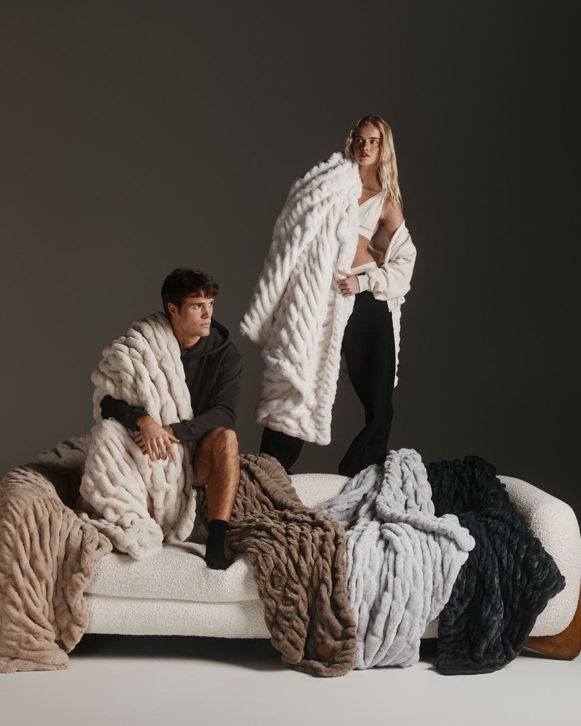 Man and woman standing on couch with blankets.