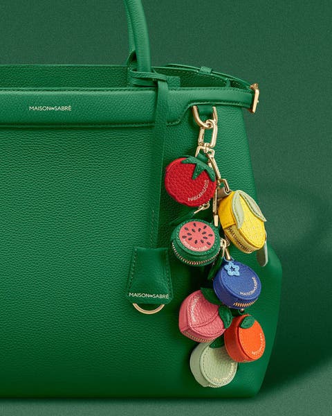 Assorted MAISON de SABRÉ bag charms on a green handbag.