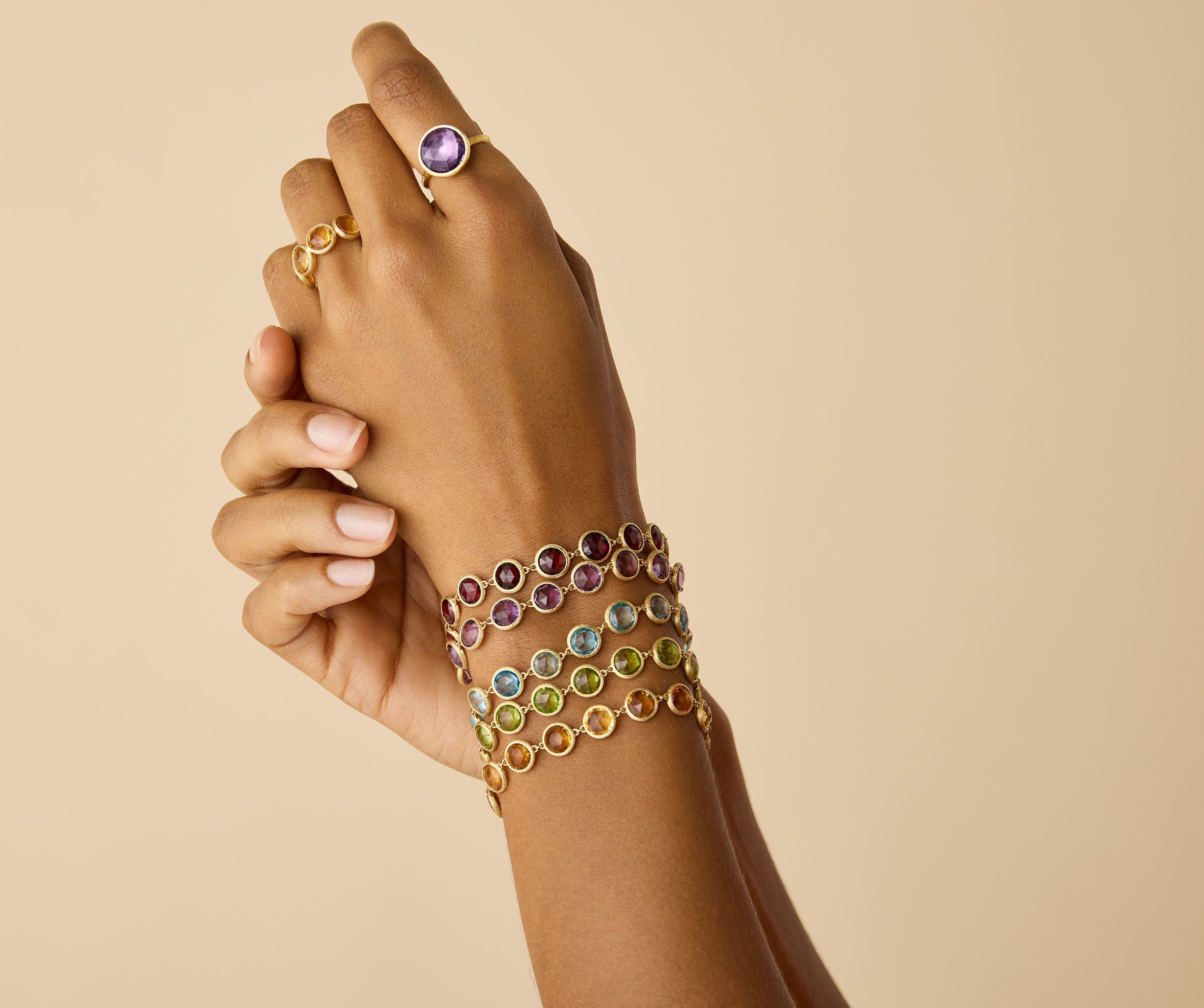 A pair of hands wearing gemstone bracelets and rings. 