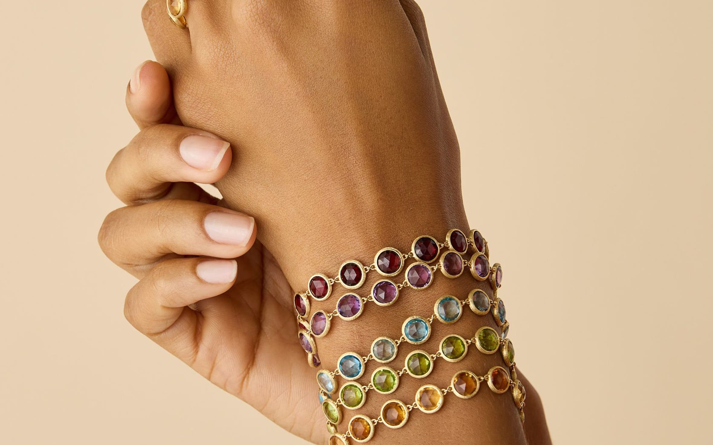 A pair of hands wearing gemstone bracelets and rings.