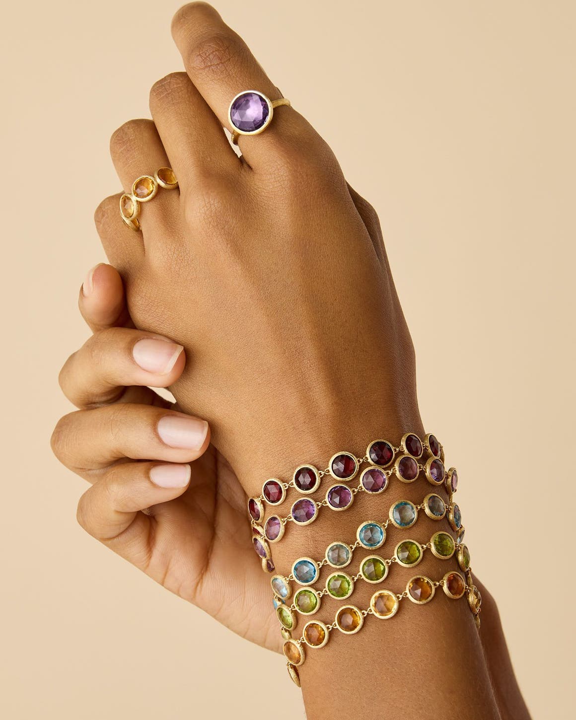 A pair of hands wearing gemstone bracelets and rings.