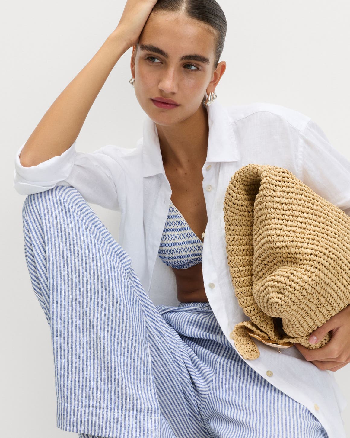 A woman wearing a button up and striped pants holding a straw bag.