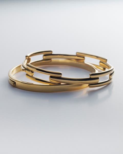 Two gold Monica Vinader bangles stacked on top of each other.