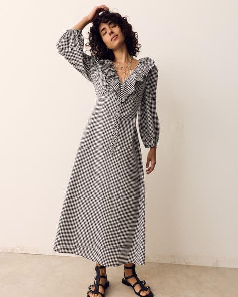 A woman wearing a black and white dress with ruffled collar and sandals.