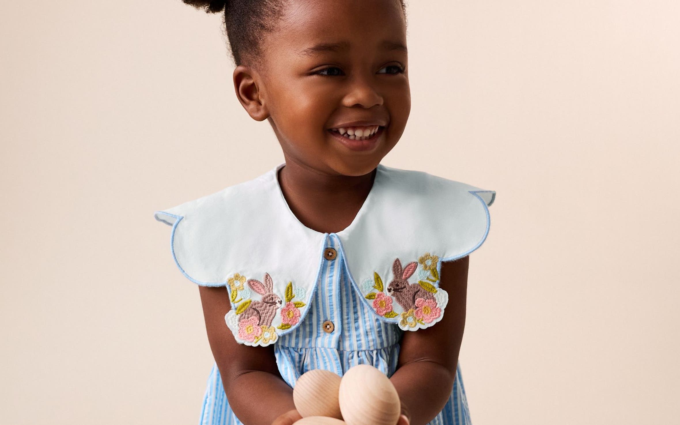 A little girl wearing a light blue dress with embroidered statement collar.