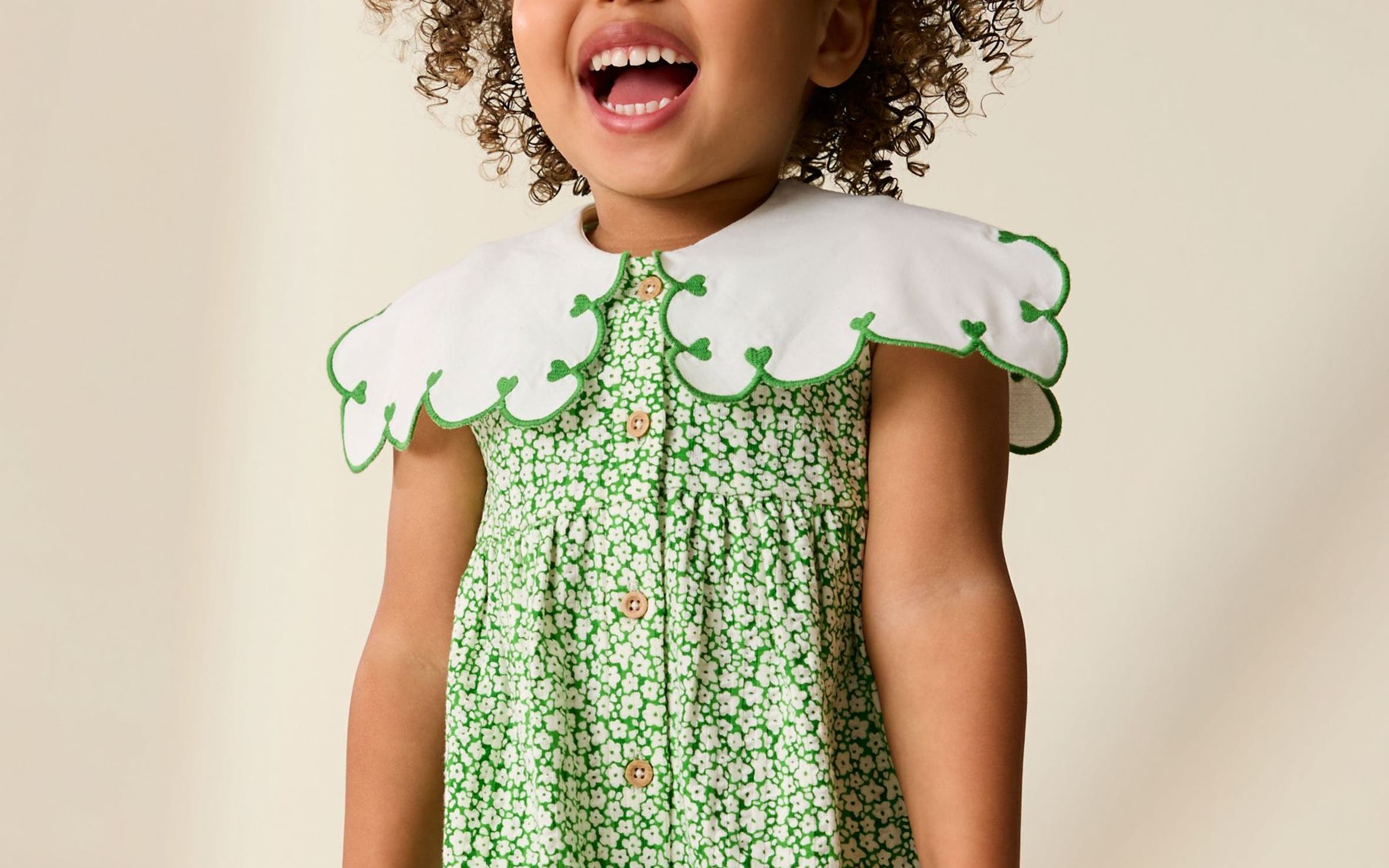 A girl wearing a green floral dress with a scalloped collar.