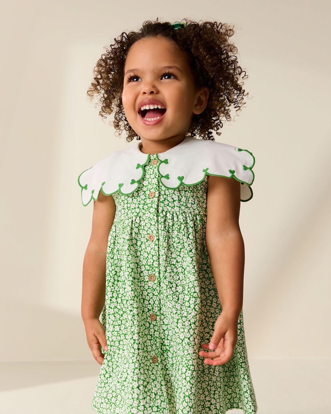 A girl wearing a green floral dress with a scalloped collar.