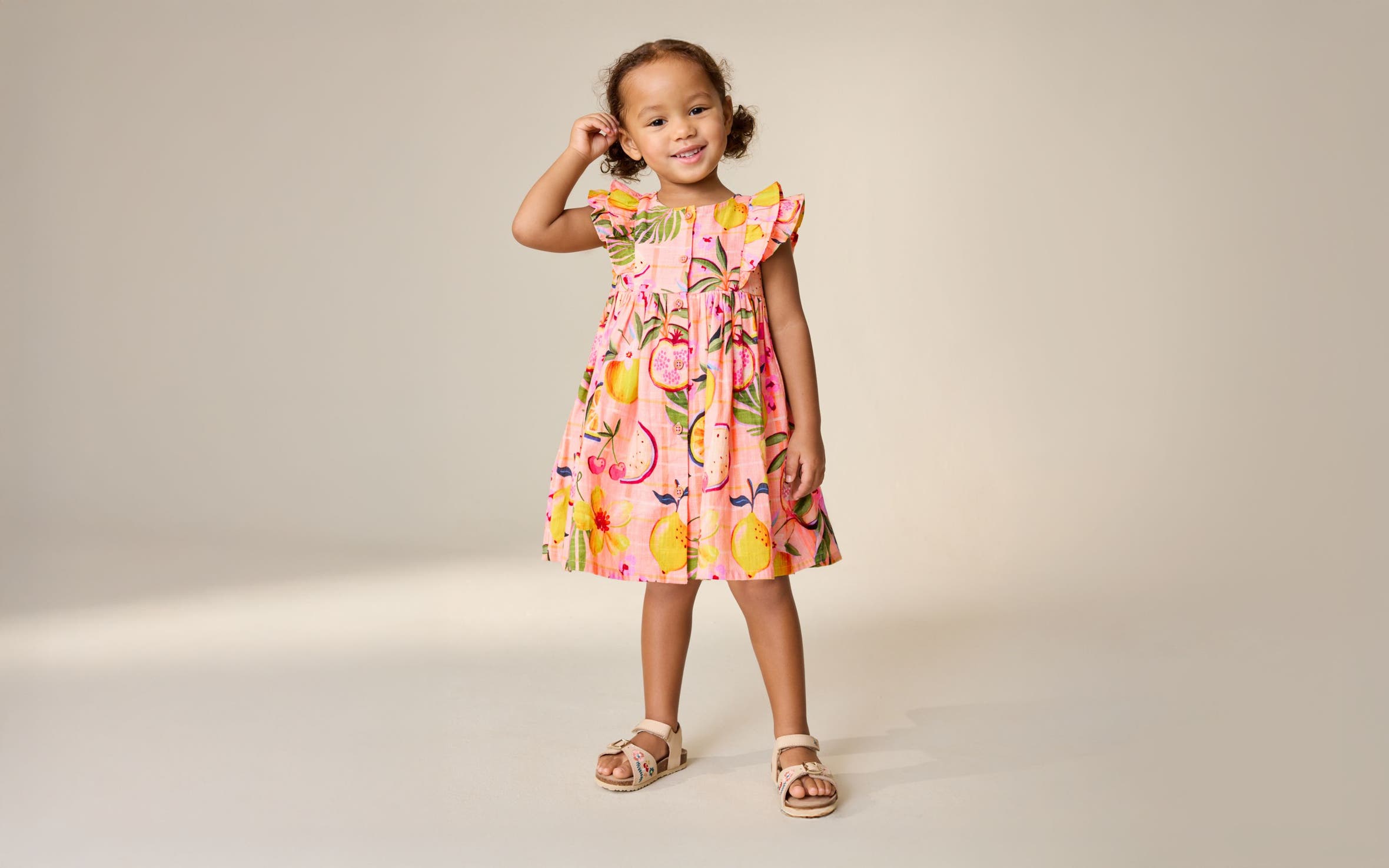 A little girl wearing a fruit-print sundress from Next.