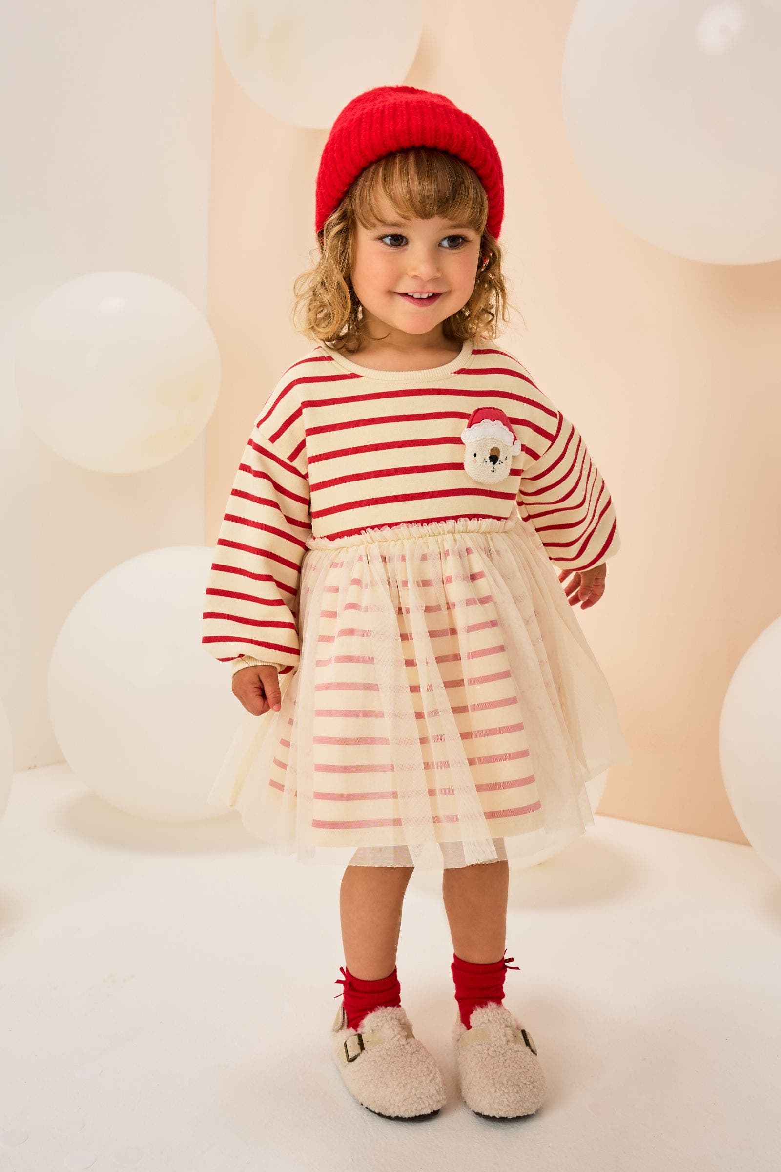 A little girl wearing a red striped dress with a Santa appliqué.