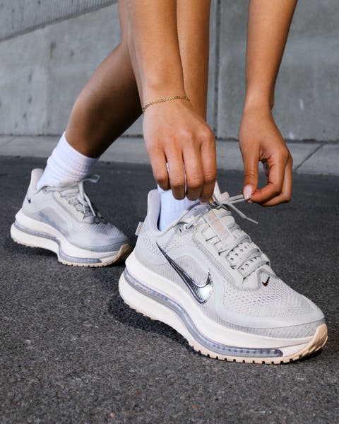 N125 exclusive; a woman wearing white Nike running shoes with silver trim.