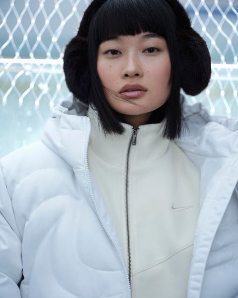 Woman wearing black earmuffs and white Nike puffer over a creme Nike zip up