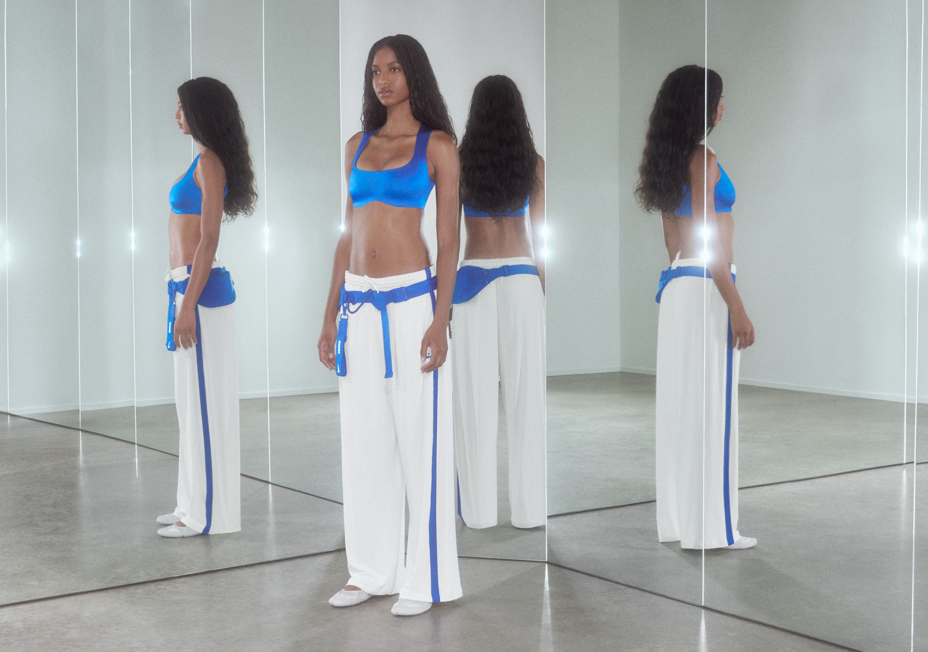 A woman wearing a blue sports bra and white track pants.
