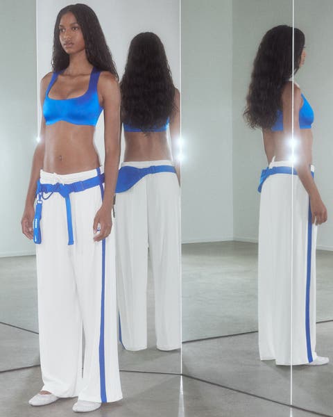 A woman wearing a blue sports bra and white track pants.