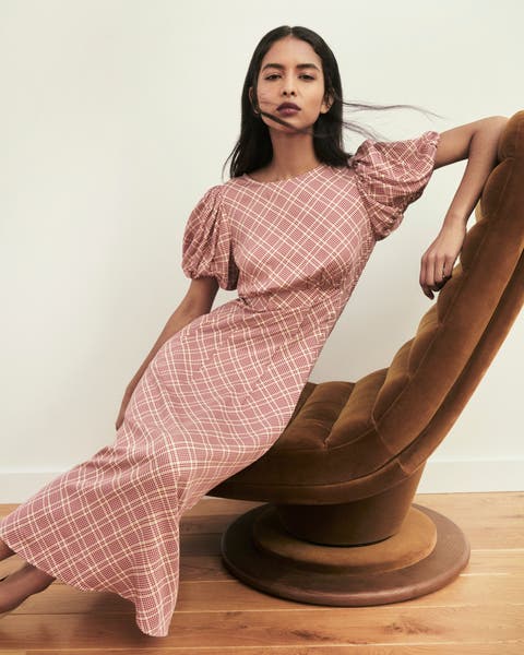A woman in pink gingham dress, seated in a brown chair.