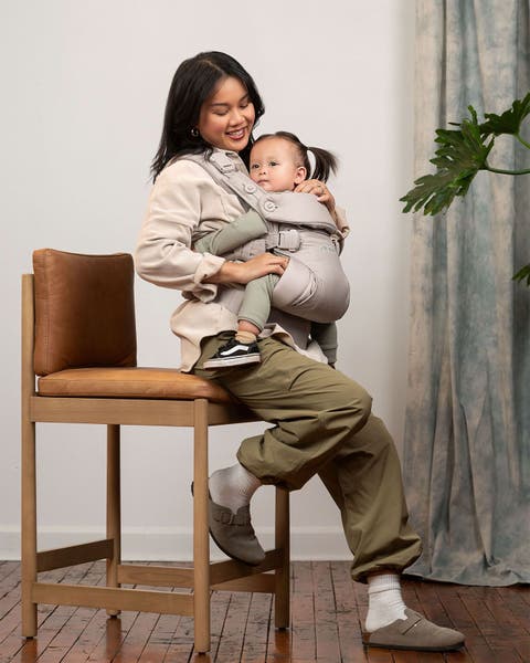 Mother holding her child close via a baby carrier by Nuna.