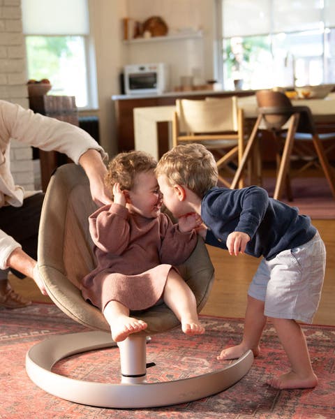 Two siblings pictured with youngest seated in the Nuna LEAF grow baby seat.