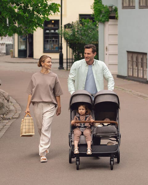 Couple walking with child in a double stroller by Nuna.