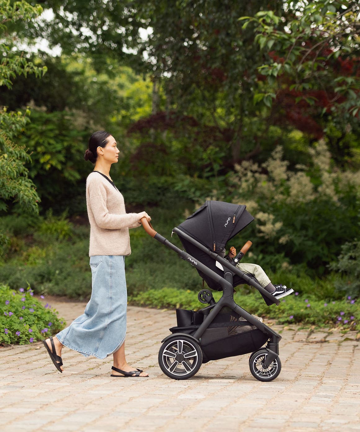 A woman pushing a child in a Nuna stroller.