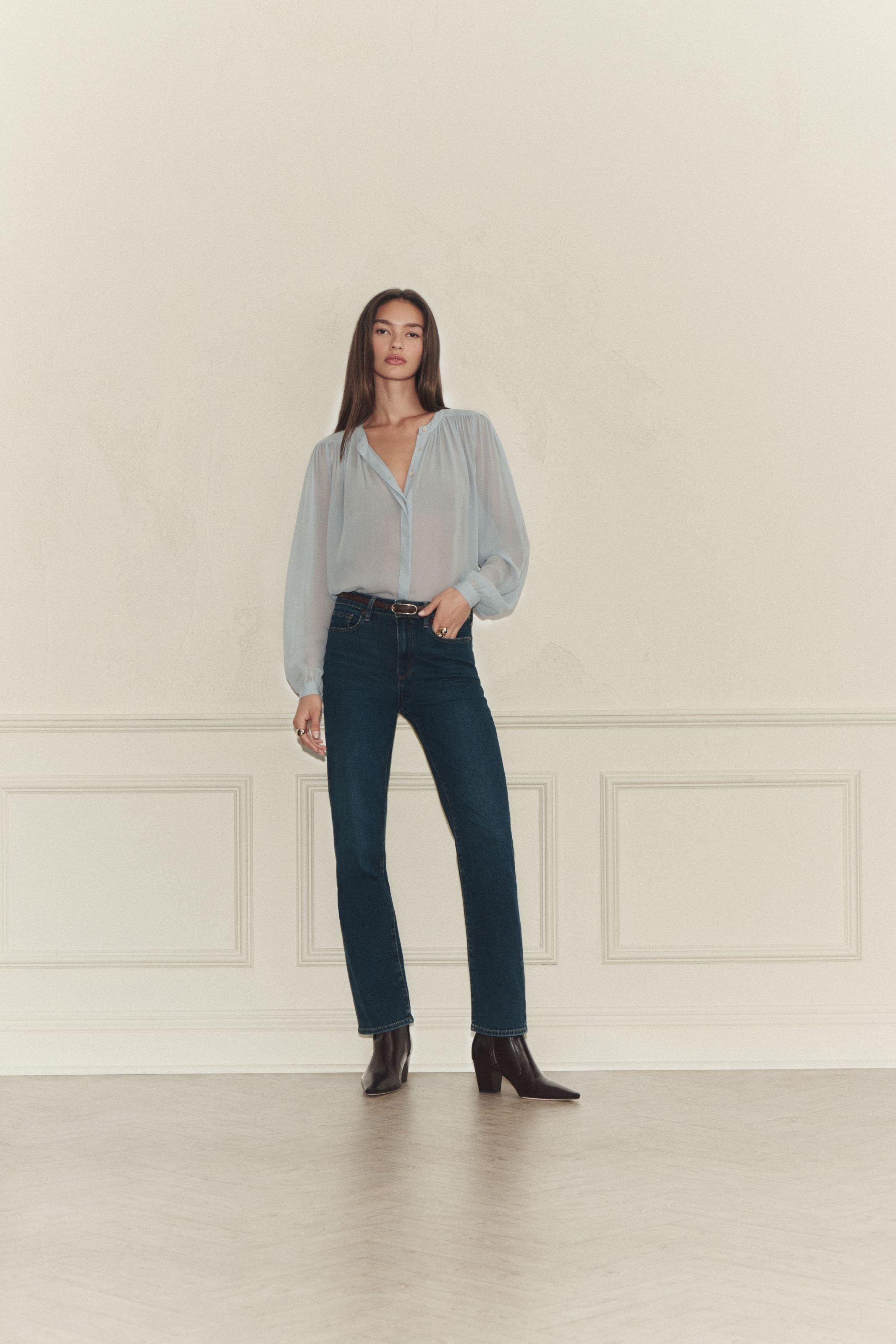 A woman wearing a sheer blue blouse and dark wash jeans.