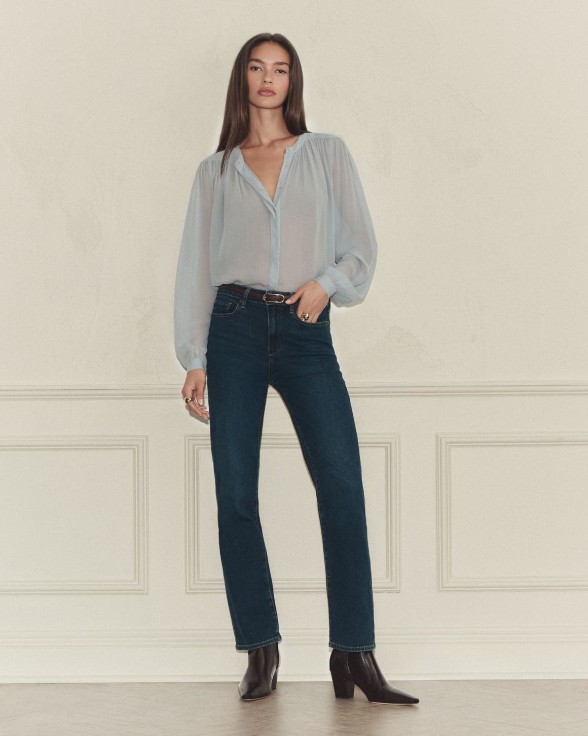 A woman wearing a sheer blue blouse and dark wash jeans.