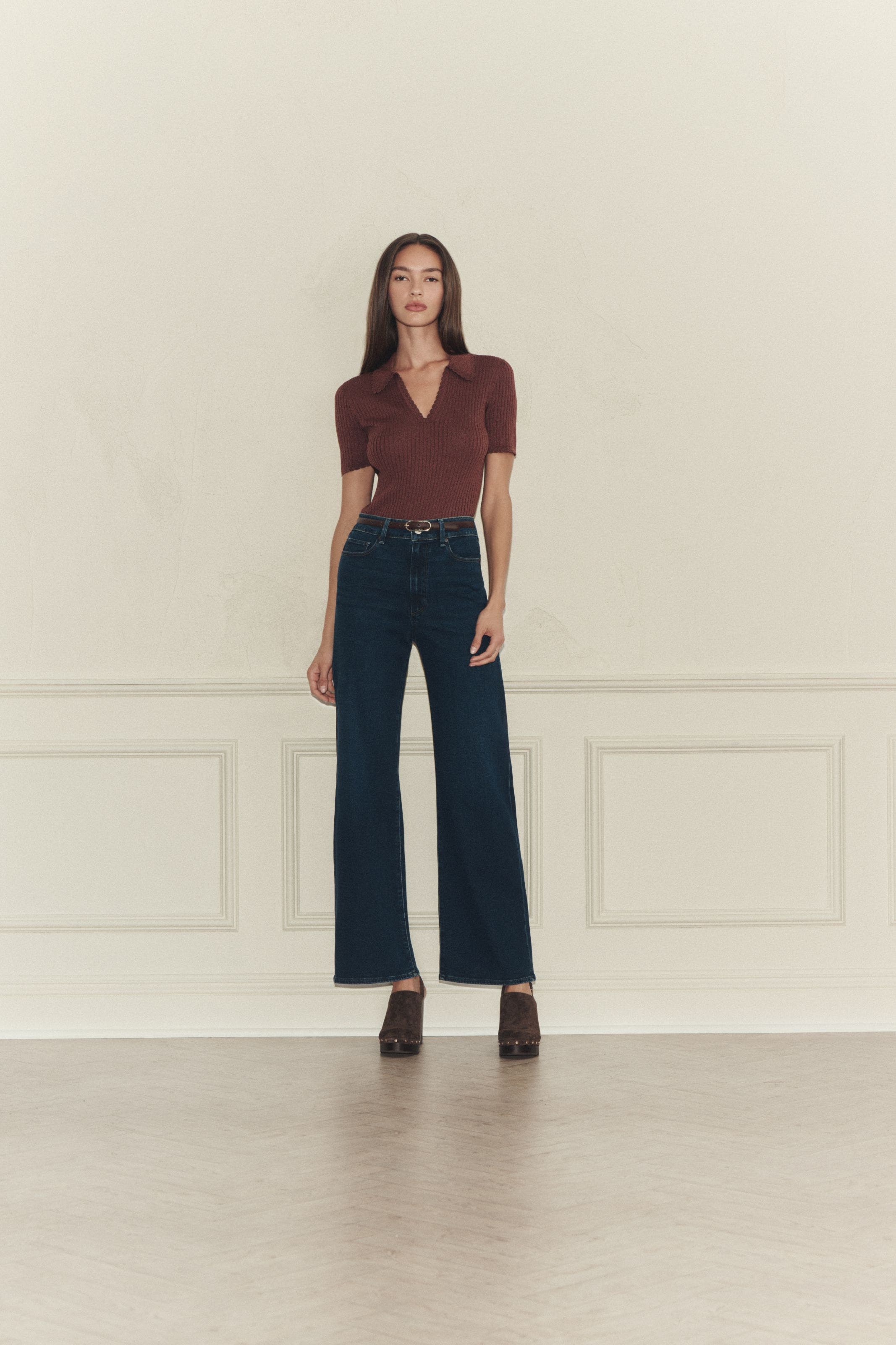 A woman wearing a brown polo sweater and dark wash jeans.