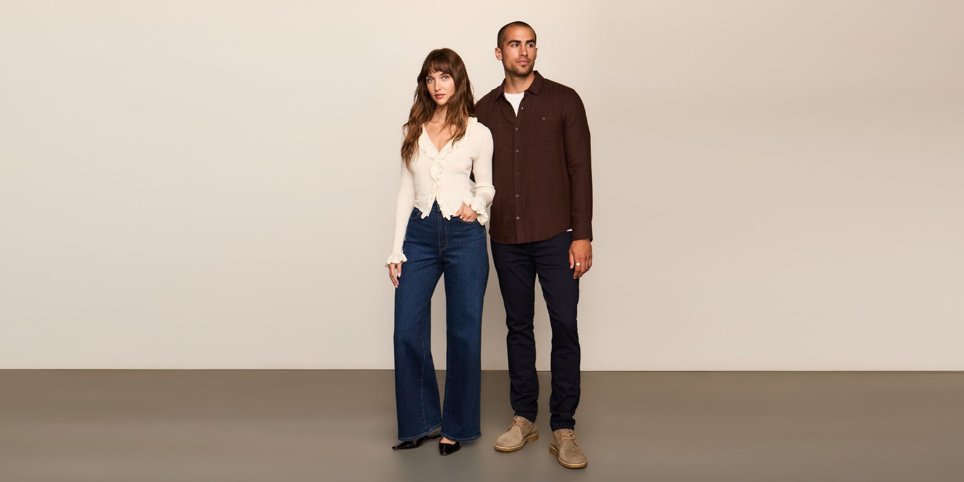 A man in black jeans and maroon button up standing next to a woman in a white top and dark denim.