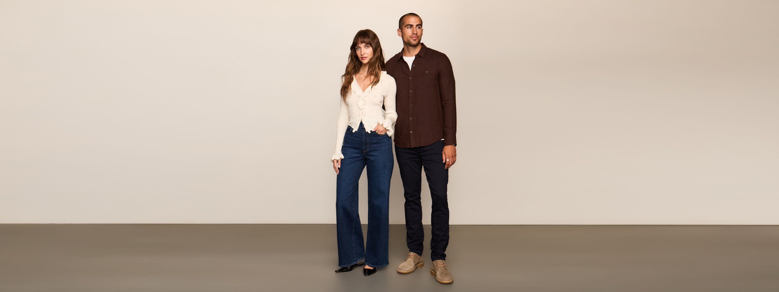 A man in black jeans and maroon button up standing next to a woman in a white top and dark denim.