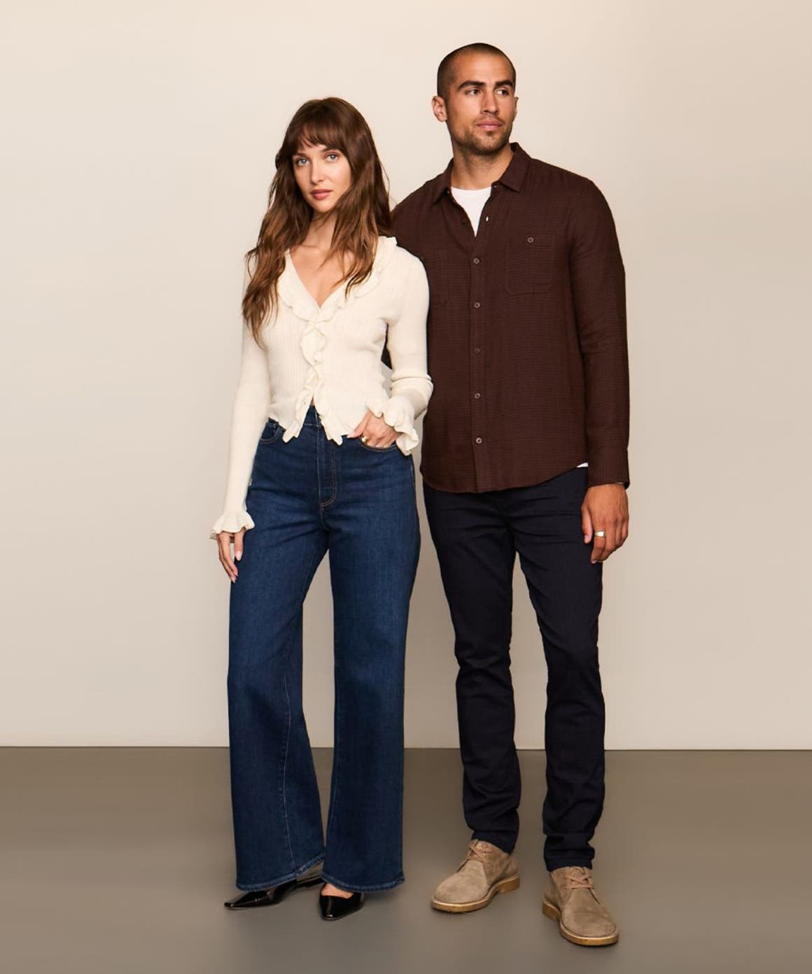 A man in black jeans and maroon button up standing next to a woman in a white top and dark denim.